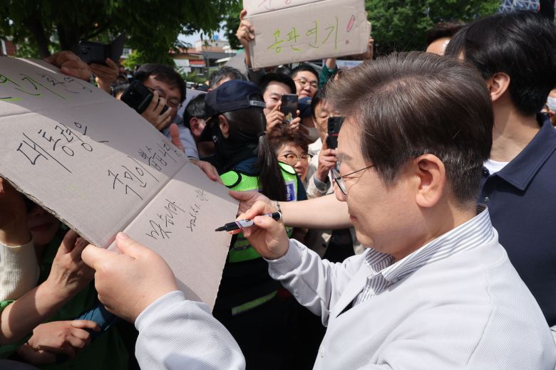 이재명 더불어민주당  대선 후보가 ‘골목골목 경청투어:국토종주편’에 나선 7일 전북 전주시 풍남문 앞 광장에서 지지자들에게 인사를 하던 도중 한 지지자가 든 ‘공판 연기 환영, 대통령은 국민이 뽑습니다’라는 팻말에 사인을 하고 있다. [연합]