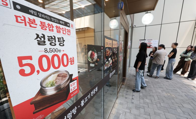 13일 할인 안내문이 붙은 서울 시내 한 인생설렁탕 매장에서 시민들이 줄을 서고 있다. [연합]