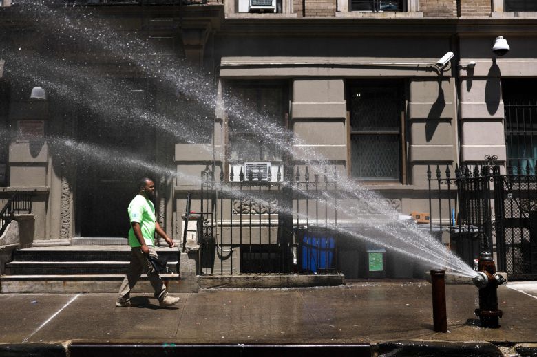 25일(현지시간) 뉴욕시 맨해튼 자치구에서 한 남성이 물을 뿌리는 소화전을 지나고 있다. [AFP]