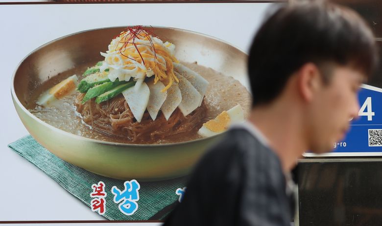 서울 마포구의 한 식당에 붙은 냉면 메뉴 사진 앞으로 시민이 지나고 있다.  [연합]