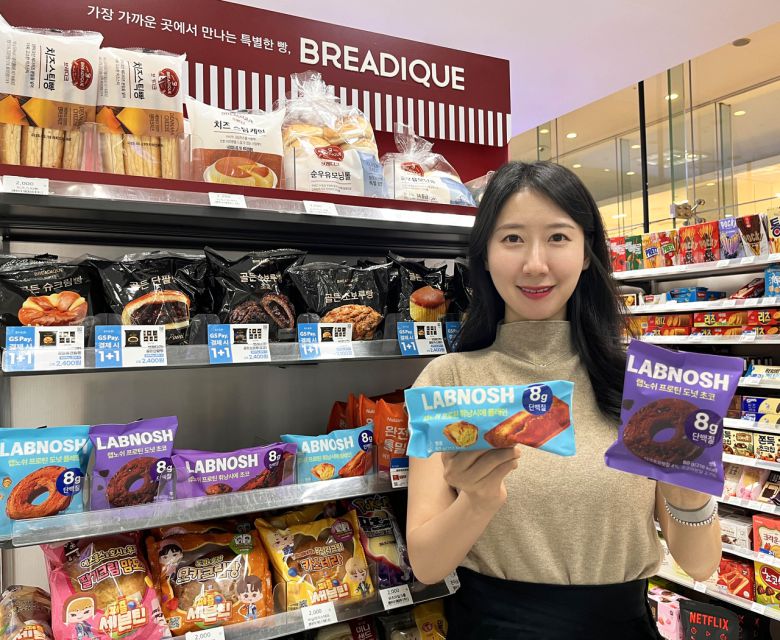 GS25에서 모델이 신상품 랩노쉬 프로틴 휘낭시에 플레인, 랩노쉬 프로틴 도넛 초코를 들고 포즈를 취하고 있다. 사진은 이번 리콜 조치와 무관함 [GS리테일 제공]