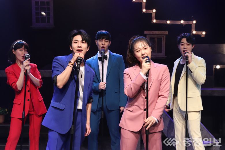 화려한 조명 아래 다섯 명의 배우가 각기 다른 색의 슈트를 입고 무대 중앙에서 노래를 부르고 있다