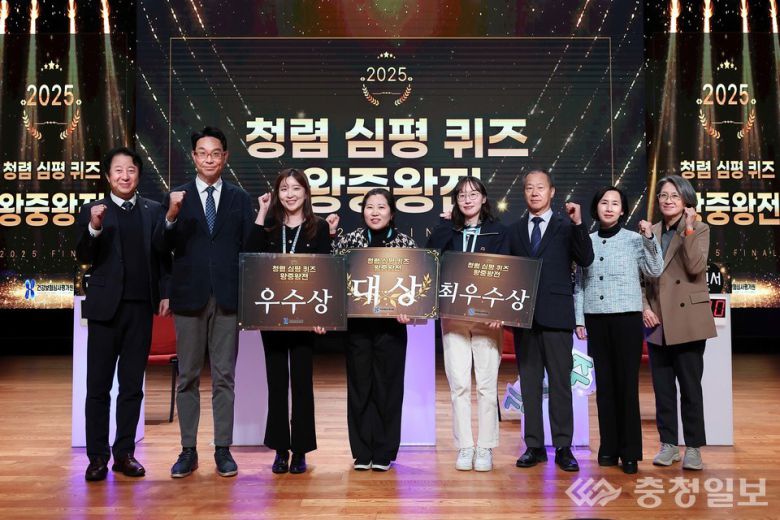 2025년 12월 4일, 건강보험심사평가원이 본원 컨퍼런스 홀에서 개최한 ‘2025 청렴 심평 퀴즈 왕중왕전’에서 수상자들이 관계자들과 함께 기념 포즈를 취하고 있다. 중앙에는 대상 수상자인 부산본부 김영숙 과장이 자리하고 있으며, 양옆으로 우수상과 최우수상 수상자가 상패를 들고 서 있다. 참석자들은 청렴 실천 의지를 상징하듯 주먹을 들어 보이며 행사 의미를 함께 나누고 있다