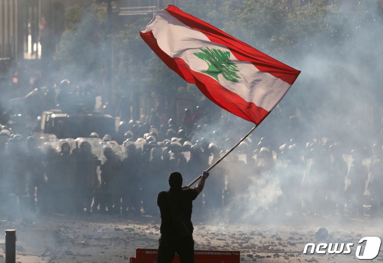 8일 한 시위대가 레바논 국기를 들고 반정부 시위를 벌이고 있다. 경찰은 최루탄으로 시위대를 진압하고 있다. © 로이터=뉴스1 © News1 박형기 기자