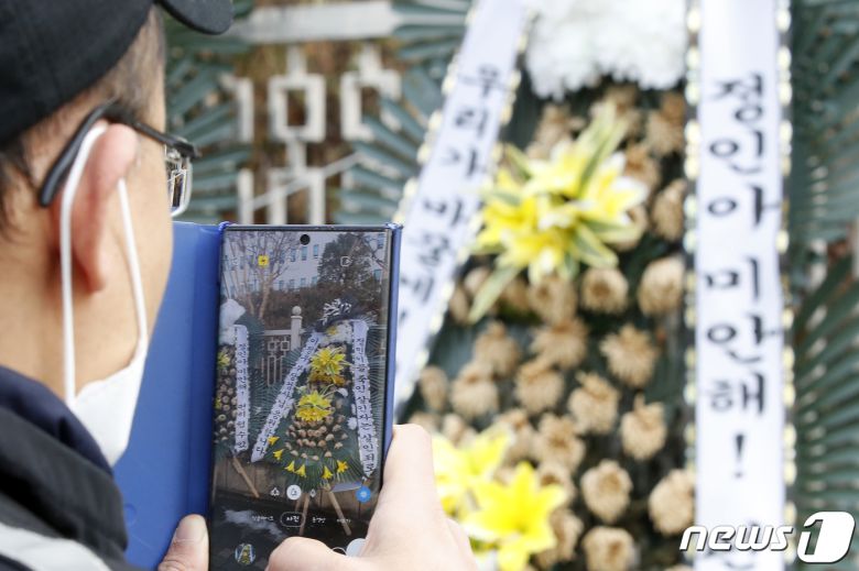 정인양을 입양한 후 수개월간 학대해 사망에 이르게 한 혐의를 받는 양부모에 대한 첫 재판이 열린 13일 오후 서울 양천구 서울남부지방법원 앞에서 한 시민이 정인이를 추모하는 조화를 촬영하고 있다. 서울남부지법 형사합의13부(부장판사 신혁재)는 이날 아동학대범죄의 처벌 등에 관한 특례법 위반(아동학대치사) 등으로 구속기소된 양모 장모씨와 아동복지법위반(아동유기‧방임) 등 혐의로 재판에 넘겨진 양부 안모씨를 대상으로 첫 공판기일을 진행했으며, 재판 과정에서 기존에 알려지지 않은 학대 정황이 추가로 드러났다고 알려졌다. 2021.1.13/뉴스1 © News1 이승배 기자