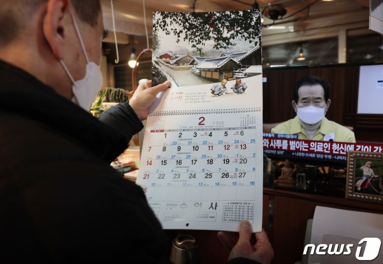 정부가 현행 사회적 거리두기 단계를 설 연휴가 끝날 때까지 2주 더 연장하겠다고 밝힌 31일 서울 광장시장에서 한 상인이 TV로 거리두기 연장 발표를 시청하며 2월달 달력을 살펴보고 있다. 이날 정세균 총리는 자영업자·소상공인들에게는 “송구하다”는 입장을 전하며 “조금만 더 힘내 달라”고 호소했다. 2021.1.31/뉴스1 © News1 이성철 기자