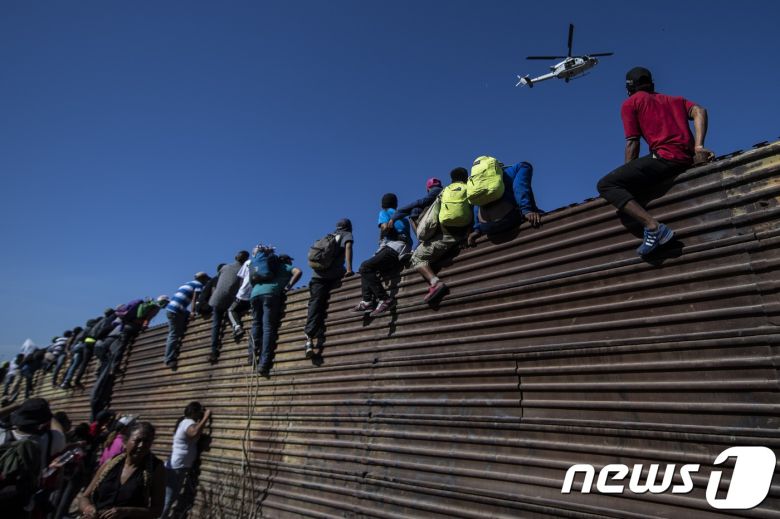 25일(현지시간) 멕시코 티후아나에 도착한 중미 이민자(캐러밴)들이 미국-멕시코 국경 펜스 위로 올라가고 있다. © AFP=뉴스1 © News1 우동명 기자