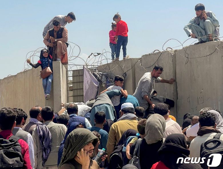 아프가니스탄 카불 국제공항에 진입하기 위해 민간인들이 담장을 넘고 있다. © 로이터=뉴스1 © News1 정윤영 기자