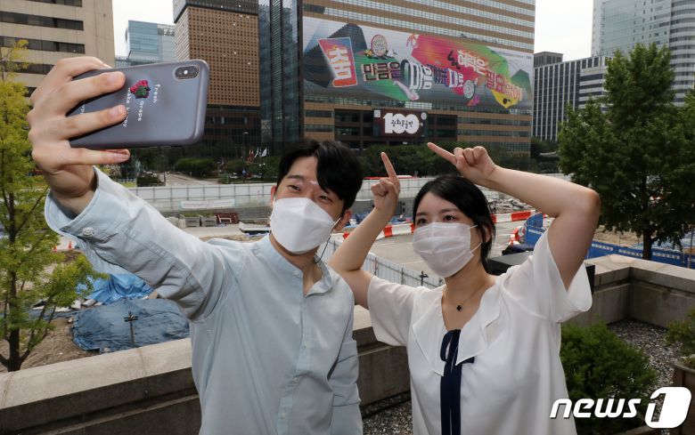 30일 오전 서울 종로구 교보빌딩에 100번째 광화문글판 '춤 만큼은 마음 가는 대로, 허락은 필요 없어'을 배경으로 시민들이 사진을 찍고 있다. 글로벌 아티스트 방탄소년단(BTS)가 100번째 광화문글판을 위해 문안 제작에 참여한 이번 글판은 코로나 펜데믹으로 제약이 늘고 고단한 하루 속에서도 허락받지 않고 자유로움을 느낄 수 있는 것을 찾자는 메시지를 담았다. 2021.8.30/뉴스1 © News1 박세연 기자