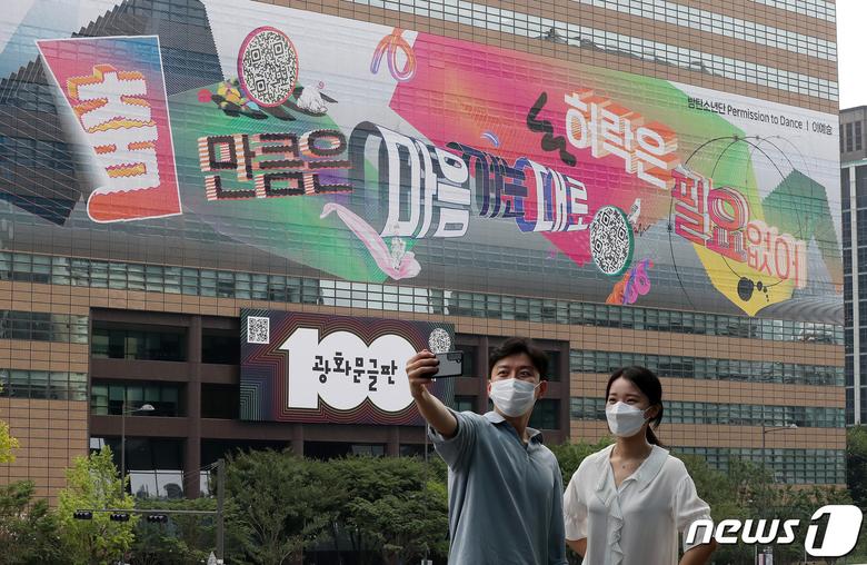 30일 오전 서울 종로구 교보빌딩에 100번째 광화문글판 '춤 만큼은 마음 가는 대로, 허락은 필요 없어'을 배경으로 시민들이 사진을 찍고 있다. 글로벌 아티스트 방탄소년단(BTS)가 100번째 광화문글판을 위해 문안 제작에 참여한 이번 글판은 코로나 펜데믹으로 제약이 늘고 고단한 하루 속에서도 허락받지 않고 자유로움을 느낄 수 있는 것을 찾자는 메시지를 담았다. 2021.8.30/뉴스1 © News1 박세연 기자