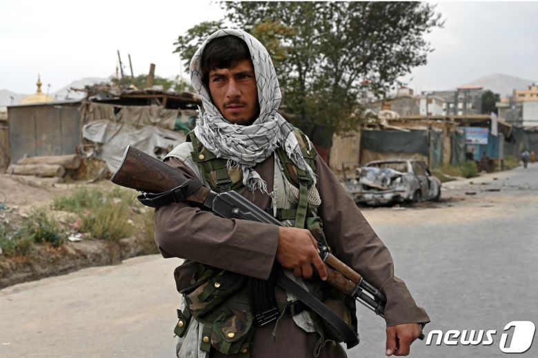 30일 아프간 수도 카불에서 로켓 공격으로 손상된 자동차 인근을 지키고 있는 탈레반 대원. © AFP=뉴스1
