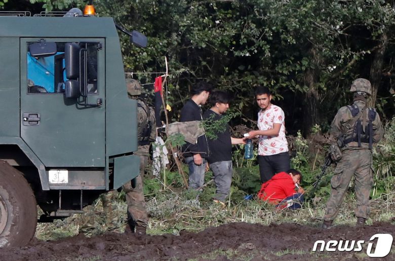 폴란드 국경수비대 장교들이 우스나르즈 고르니 마을 인근 벨라루시와 폴란드 국경에서 고립된 한 무리의 이주자들 옆에서 경계를 서고 있다. © 로이터=뉴스1