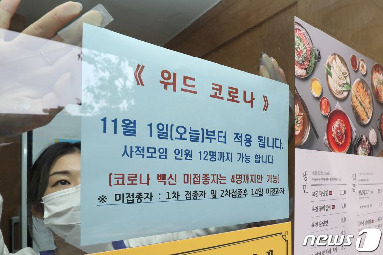 단계적 일상회복(위드 코로나) 시행 첫날인 1일 대구 중구의 한 음식점 관계자가 점심시간을 앞두고 유리창에 최대 12명 모임 가능 안내문을 붙이고 있다. 2021.11.1/뉴스1 © News1 공정식 기자