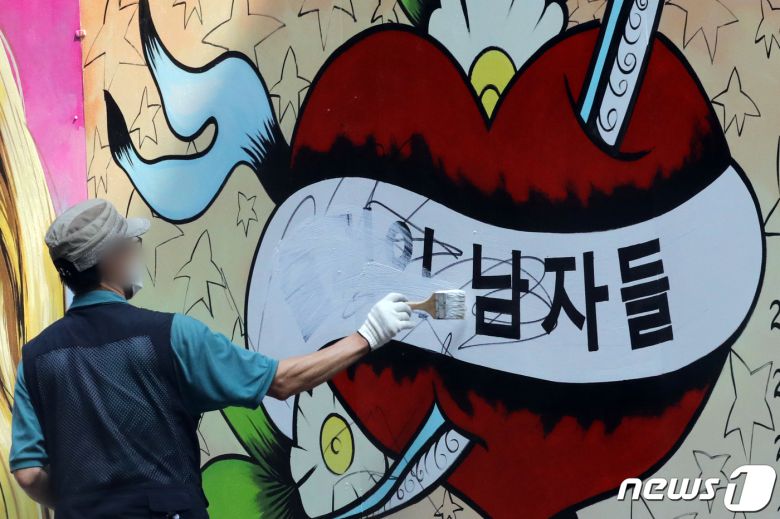 30일 오전 서울 종로구의 한 서점 벽면에 그려진 윤석열 전 검찰총장의 배우자 김건희 씨를 비방하는 내용의 벽화 문구를 서점 관계자가 페인트로 지우고 있다. 2021.7.30/뉴스1 © News1 황기선 기자