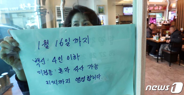 31일 서울 종로구 한 식당에서 종업원이 거리두기 연장관련 문구를 붙이고 있다. 이날 정부는 사적모임 인원을 최대 4명까지 허용하고 식당·카페 등은 오후 9시까지로 영업시간을 제한하는 현 거리두기 조치를 2주간 연장한다고 발표했다. 2021.12.31/뉴스1 © News1 김명섭 기자