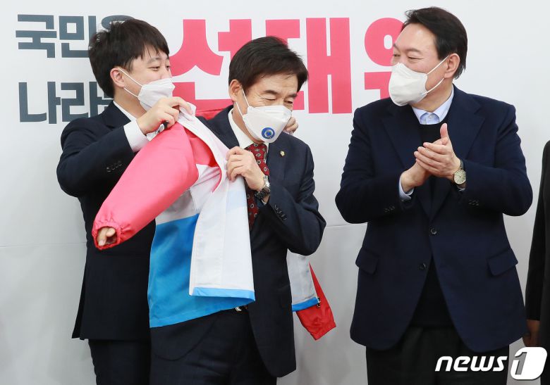 이준석 국민의힘 대표(왼쪽)가 7일 오후 서울 여의도 국회에서 국민의힘에 입당한 이용호 의원(가운데)에게 당복을 입혀주고 있다. 오른쪽은 윤석열 대선후보. 이 의원은 2004년 새천년민주당 후보로 17대 국회의원 선거에 출마했지만 낙선했고, 2016년 20대 총선에서는 국민의당 후보로 전북 남원·순창·임실 지역구에서 당선됐다. 이후 국민의당과 바른정당의 합당에 반발하며 탈당했으며, 21대 총선에서는 호남에서 비(非) 민주당 후보로는 유일하게 재선에 성공한 바 있다. 2021.12.7/뉴스1 ⓒ News1 이동해 기자