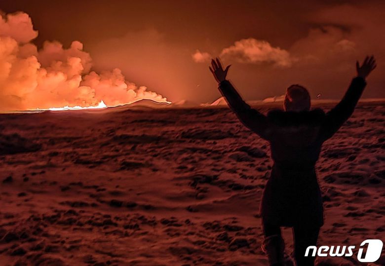 18일(현지시간) 아이슬란드 남서부 레이캬비크반도에서 화산이 분화하며 화산재를 내뿜고 있는 가운데 지역 주민이 이 광경을 바라보며 두 손을 들고 있다. 2023.12.18 ⓒ AFP=뉴스1 ⓒ News1 정지윤 기자