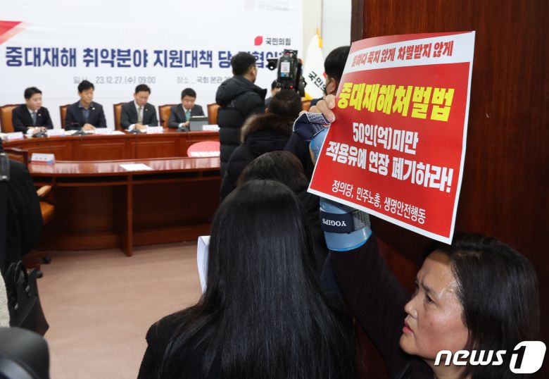 고 김용균씨 어머니 김미숙씨가 27일 서울 여의도 국회에서 열린 중대재해 취약분야 지원대책 관련 당정협의회 회장 앞에서 '중대재해처벌법 적용유예연장 폐기' 손 피켓을 들고 있다. 2023.12.27/뉴스1 ⓒ News1 송원영 기자