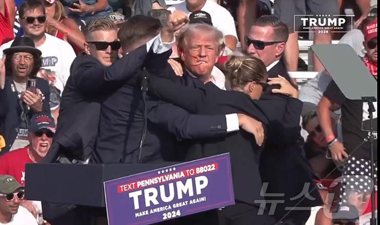 미국 공화당 대선 후보인 도널드 트럼프 전 대통령이 13일 오후(현지시간) 펜실베이니아주 버틀러에서 유세를 벌이던 중 유세장 주변에서 여러 발의 총격이 발생하면서 유세가 중단됐다. 트럼프 전 대통령은 유세를 하던 중 총소리를 듣자 곧바로 몸을 연단 밑으로 숨겼고 경호원들의 보호를 받으며 무대에서 급히 대피했다. 트럼프 전 대통령은 몸을 피하면서 지지자들에게 주먹을 들어 보이며 건재함을과시 했다..(유튜브 캡처)2024.7.14/뉴스1