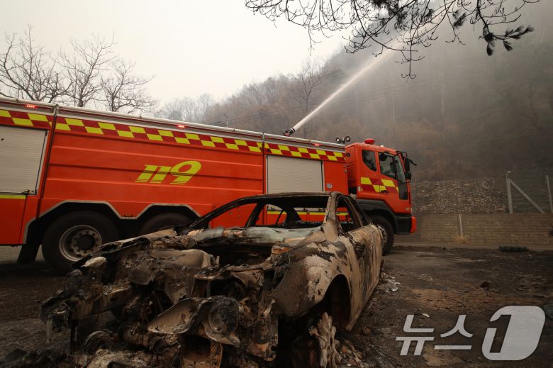 경남 산청 대형 산불이 사흘째로 접어든 23일 오전 산청군 시천면 일대에서 소방이 산불로 인해 전소된 승용차 뒤로 잔불을 정리하고 있다. ⓒ News1 윤일지 기자