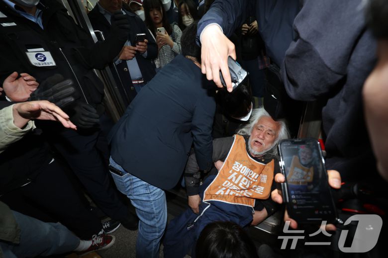 박경석 전국장애인차별철폐연대(전장연) 대표가 21일 서울 지하철 4호선 혜화역 동대문 방면 승강장에서 제62차 '출근길 지하철 탑니다' 시위를 벌이던 중 이를 저지하던 경찰·서울교통공사 직원 등과 충돌하며 열차 입구에 넘어져 있다. 2025.4.21/뉴스1 ⓒ News1 이동해 기자