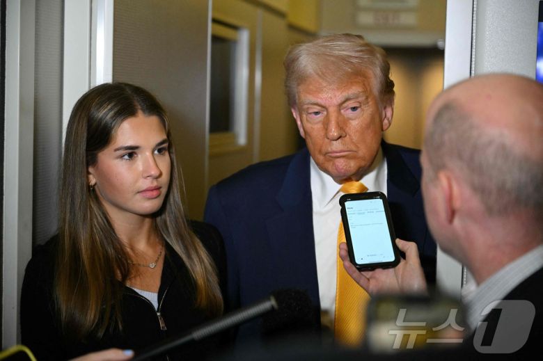 도널드 트럼프 미국 대통령이 13일(현지시간) 마이애미에서 팜비치로 향하는 에어포스원에서 기자의 질문에 답하는 동안 손녀 카이 트럼프가 그 옆에서 듣고 있다. 2025.04.13.  ⓒ AFP=뉴스1