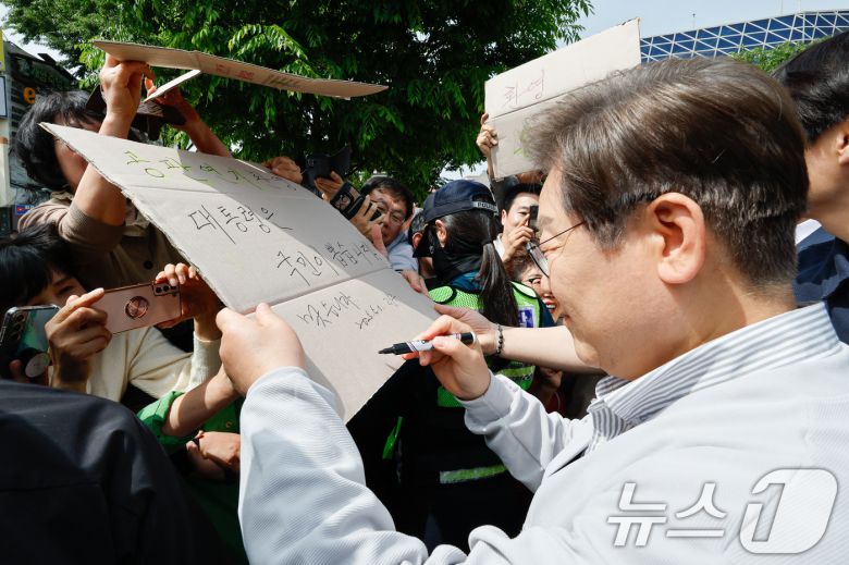 이재명 더불어민주당 대통령 후보가 2차 골목골목 경청투어 마지막 날인 7일 오후 전북 전주시 풍남문 앞에서 '공판연기 환영 대통령은 국민이 뽑습니다'라는 종이를 든 지지자에게 '맞습니다'라며 사인해주고 있다. 2025.5.7/뉴스1 ⓒ News1 안은나 기자