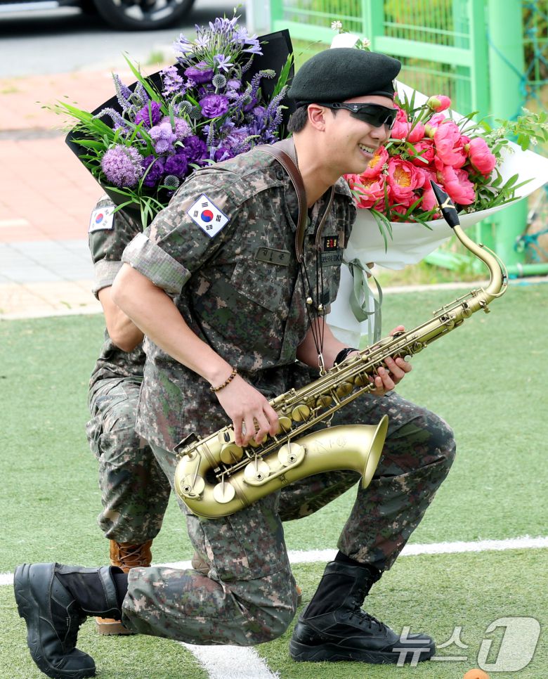 방탄소년단(BTS)의 뷔(김태형, 29)가 10일 오전 강원도 춘천시 신북읍 체육공원 축구장에서 섹소폰 연주를 하는 RM 뒤에서 꽃다발을 들고 그의 제대를 축하하고 있다. 2025.6.10/뉴스1 ⓒ News1 권현진 기자