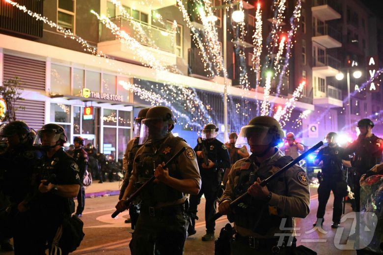 2025년 6월 9일 로스앤젤레스(LA) 시내 리틀 도쿄 인근에서 연방 이민단속 작전에 대응하는 시위 도중 진압 장비를 착용한 벤투라 카운티 보안관 사무실 소속 대원들 뒤로 폭죽이 터지고 있다. ⓒ AFP=뉴스1 ⓒ News1 신기림 기자