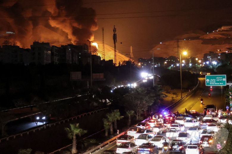 15일(현지시간) 이란 테헤란 샤란의 석유 저장고에서 이스라엘의 공습으로 인해 화재가 발생한 가운데 시민들이 차량으로 대피하고 있다.ⓒ AFP=뉴스1