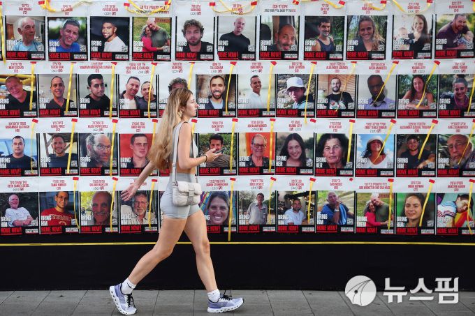 지난 8월 21일(현지시간) 이스라엘 수도 텔아비브에서 한 여성이 하마스에 인질로 납치된 피해자들 사진이 부착된 벽보 앞을 지나는 모습. [사진=로이터 뉴스핌]