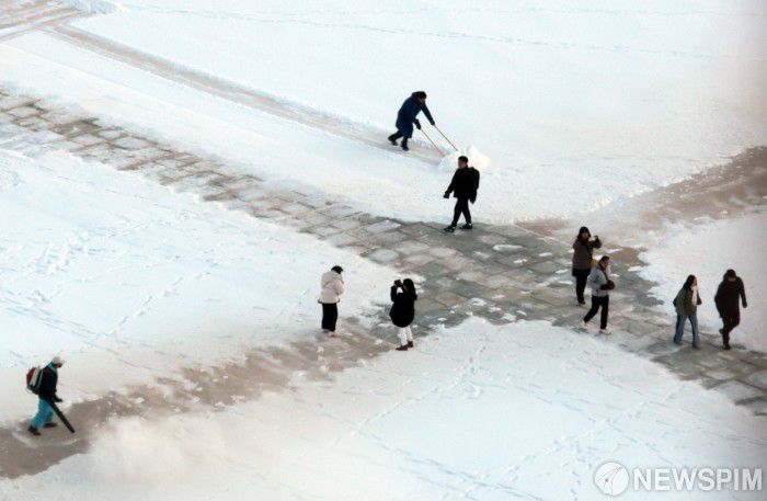 [서울=뉴스핌] 이길동 기자 =5일 오전 서울 종로구 경복궁에서 관계자들이  어젯밤 내린 눈을 치우는 가운데 관광객들이 눈을 배경으로 사진을 찍고 있다.2025.12.05 gdlee@newspim.com