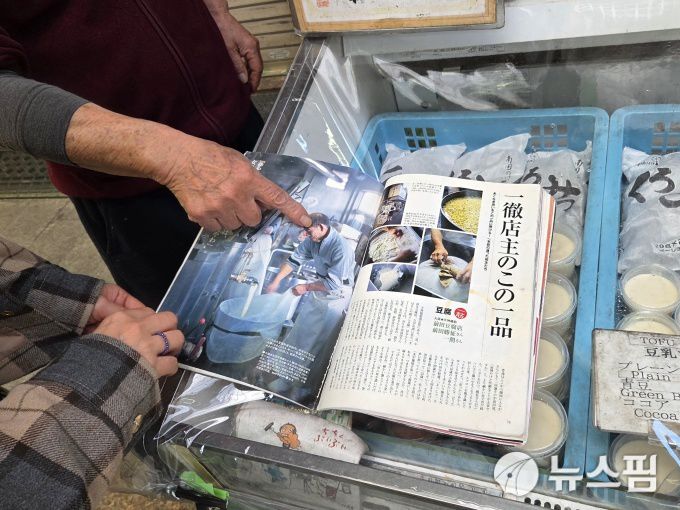 [오사카=뉴스핌] 김기랑 기자 = 일본 오사카 내 두부가게 '마에다' 점주인 마에다씨가 본인이 출연한 잡지를 가리켜보이고 있다. 2025.12.16 rang@newspim.com