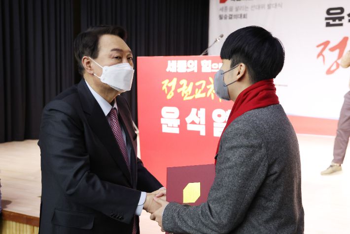 국민의힘 윤석열 대선 후보가 22일 오전 세종 비오케이아트센터에서 열린 세종 선대위 필승결의대회에서 인사말을 마친 국민의힘 제1호 청소년 당원 안상현 학생에게 빨간 목도리를 둘러주며 악수하고 있다. 연합뉴스