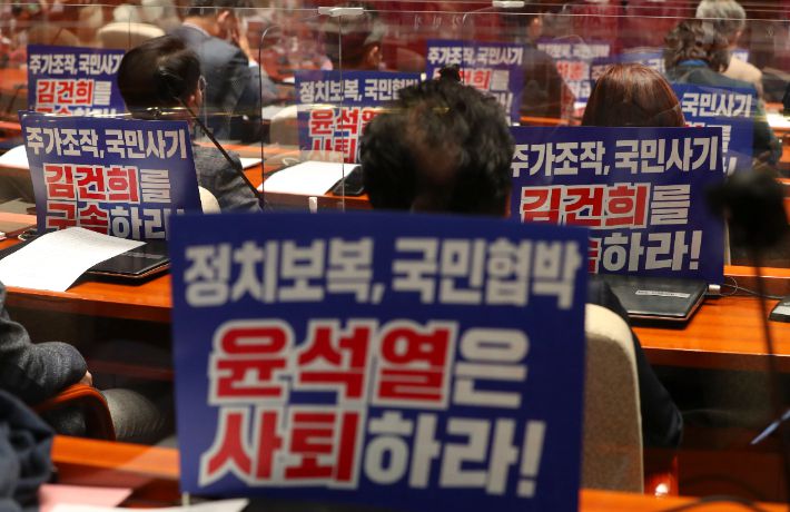 10일 서울 여의도 국회에서 열린 의원총회에 참석한 더불어민주당 의원들의 자리에 '윤석열 대선 후보 사퇴 촉구와 부인 김건희 구속 촉구' 메시지가 적힌 피켓이 붙어 있다. 2022.2.10 [국회사진기자단] 연합뉴스