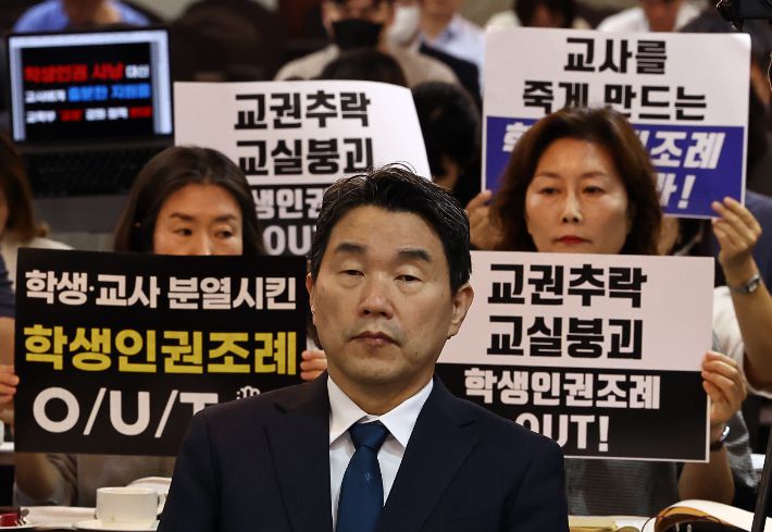 10일 오전 서울 코리아나호텔에서 열린 '교권 회복 및 보호를 위한 교육부-국가교육위원회 공동주최 토론회'에서 서울교육사랑학부모연합 등 단체가 학생인권조례 폐지를 촉구하는 피켓을 들고 있다. 앞은 이주호 부총리 겸 교육부 장관. 연합뉴스