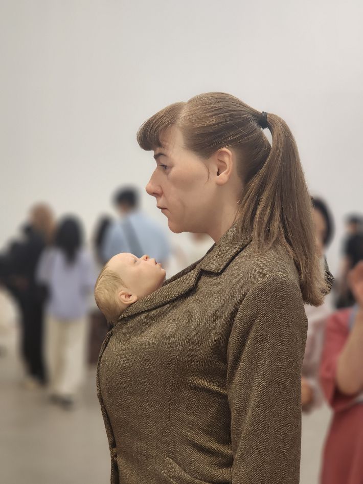 코트 안에 아이를 넣고 두 손에 주황색 비닐봉지를 들고 서 있는 '쇼핑하는 여인'(2013년작). 곽인숙 기자