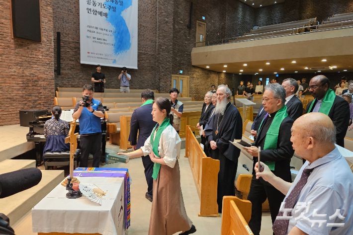 에큐메니칼 공동체 구성원들이 화해와 통일의 상징물을 들고 입장하고 있다. 개신교와 가톨릭 공동으로 번역한 남측 성경, 북측교회가 실제로 사용하는 북측 성경, 각기 다른 나무들로 만들어진 '한 몸 십자가', 물과 흙이 원래 하나이듯 분단의 아픔이 치유되길 바라는 '물과 흙'이 놓여졌다.