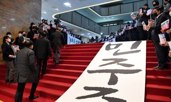 국민의힘 의원들이 10일 여의도 국회 본회의장 입구에서 본회의에 입장하는 더불어민주당 의원들을 향해 "위선정권 막장정치 민주당에 경고한다!" 등의 구호를 외치고 있다. 이날 본회의에서는 고위공직자범죄수사처(공수처) 설치 및 운영에 관한 법률 일 부개정안을 처리했다. 연합뉴스