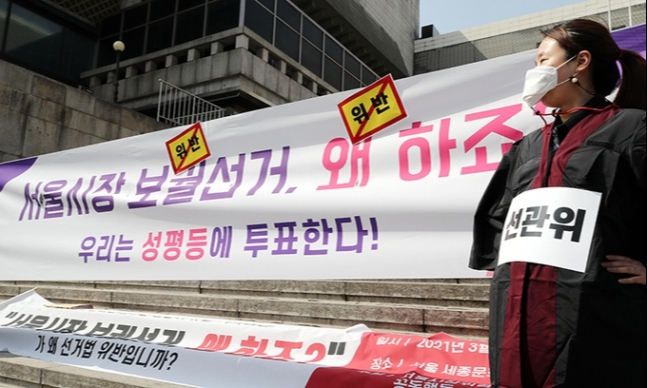 23일 오전 서울 종로구 세종문화회관 앞에서 열린 '정치참여 권리를 불허한 선관위 규탄' 기자회견에서 선관위 복장을 한 서울시장위력성폭력사건공동행동 관계자가 캠페인 문구에 위반 스티커를 붙이는 퍼포먼스를 하고 있다. 이들은 '보궐선거 왜 하죠?'라는 문구와 성평등이라는 단어를 선거법 위반이라며 사용할 수 없다고 한 서울시 선관위의 결정을 규탄했다. 연합뉴스