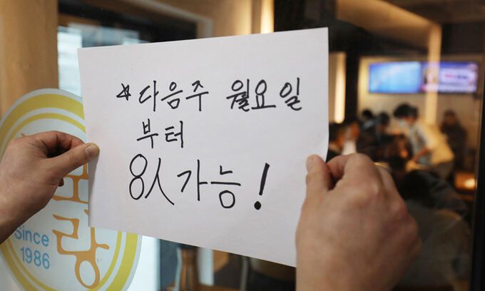 사적모임 제한이 6인에서 8인으로 조정된 18일 서울의 한 식당에서 주인이 8인 가능 안내문을 써 붙이고 있다. 서울=뉴스1