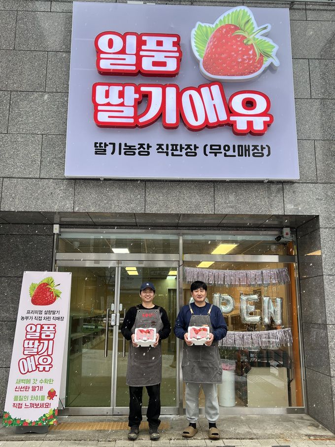‘딸기농부’ 김광훈(왼쪽)∙윤태식씨가 딸기 무인판매장 앞에서 딸기를 들고 홍보 사진을 찍고 있다. 김광훈씨 제공
