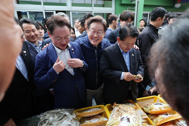 민심을 청취하는 '경청 투어'에 나선 이재명 더불어민주당 대선후보가 2일 오후 강원도 인제군 원통전통시장에서 건어물 가게를 방문해 황태채를 맛본 뒤 허영(왼쪽), 김병주 의원에게 구입을 권하고 있다.   뉴시스