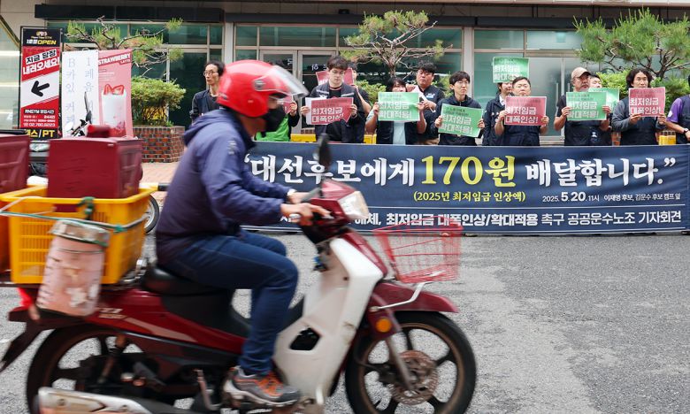 지난 20일 한 배달 노동자가 서울 여의도 이재명 더불어민주당 대선후보 캠프 앞에서 열린 민주노총 공공운수노조 조합원들이 연 '윤석열 최저임금위원회 해체, 최저임금 대폭인상과 확대적용' 촉구 기자회견 앞을 지나고 있다. 뉴스1