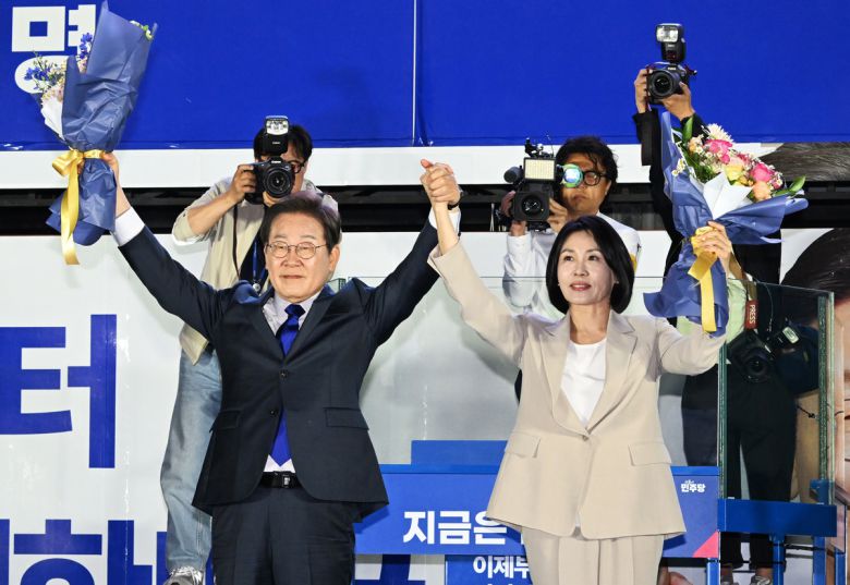 지난 4일 오전 당시 제21대 대통령 당선이 확실시되는 더불어민주당 이재명 대선 후보와 부인 김혜경 여사가 서울 여의도 국회 인근에서 당 주최로 열린 국민개표방송 행사에 참석해 꽃다발을 받고서 시민들을 향해 두 팔을 들어 인사하고 있다. 연합뉴스