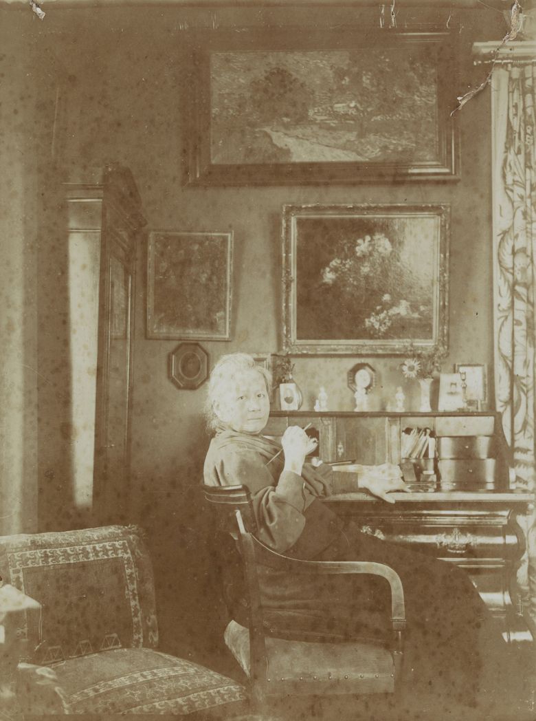 거실 책상 앞의 요 반 고흐 봉어르. 1909년 혹은 그 이후 암스테르담 집에서 찍은 사진으로 책상 뒤편 벽에 판탱라투르의 ‘꽃’과 빈센트 반 고흐의 ‘은선초 꽃병’, ‘황혼풍경(위)’이 보인다. 아트북스 제공