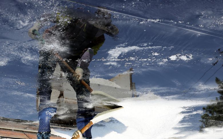 염부 전동길 씨가 결정지에서 소금삽을 들고 소금을 긁어모으고 있다. 사진은 결정지에 반영된 전동길씨 모습이다.