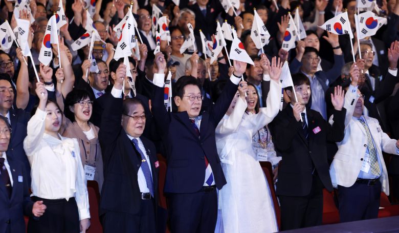 이재명 대통령과 김혜경 여사가 15일 서울 종로구 세종문화회관에서 열린 제80주년 광복절 경축식에서 참석자들과 태극기를 흔들며 만세 삼창을 하고 있다. 뉴시스