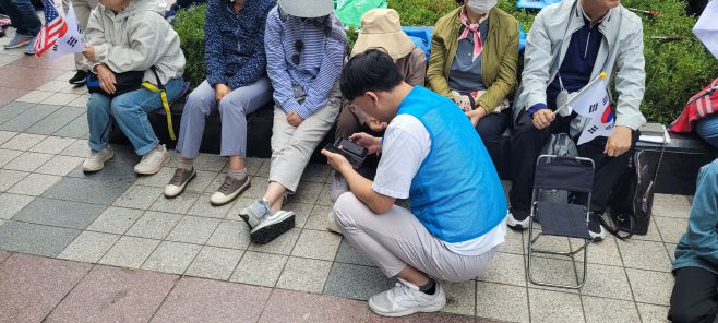 3일 오전 서울 종로구 동화면세점 앞에서 열린 '10·3 국민혁명대회'에서 파란 조끼를 입은 한 사랑제일교회 봉사단이 휴대폰 사용에 어려움을 겪는 집회 참가자 A씨를 돕고 있다. /특별취재팀