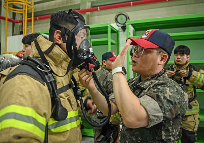 해군 3함대 손상통제훈련장에서 3훈련대대 소속 훈련관찰관들이 해양경찰관들을 대상으로 소방복과 양압식 공기호흡기 착용법을 지도하고 있다. /해군 3함대사령부